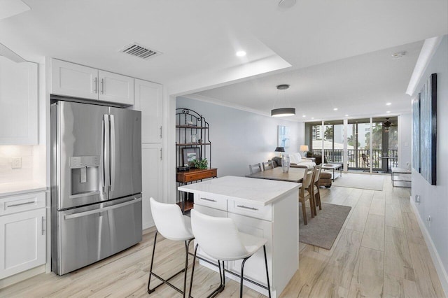 kitchen with a kitchen bar, stainless steel refrigerator with ice dispenser, light wood-type flooring, light stone counters, and white cabinetry