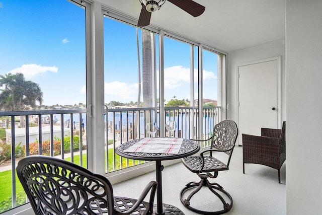 sunroom with ceiling fan and a water view