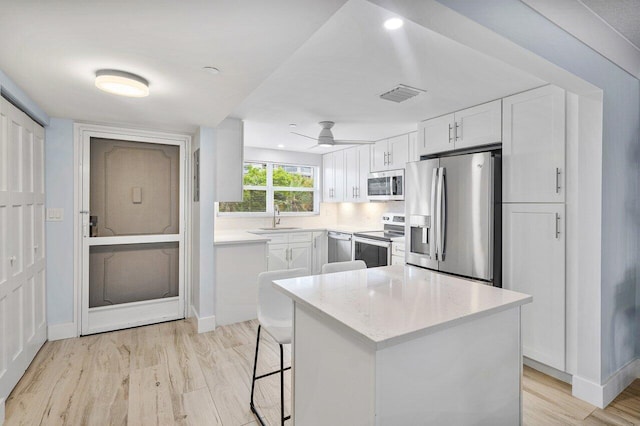 kitchen with a center island, white cabinets, sink, light hardwood / wood-style flooring, and stainless steel appliances