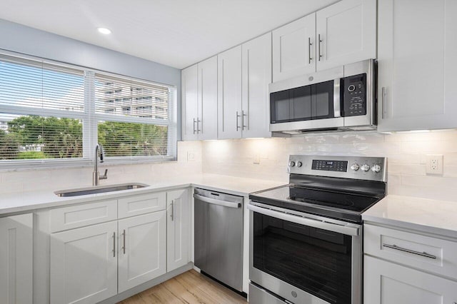 kitchen with white cabinets, sink, light hardwood / wood-style flooring, light stone countertops, and appliances with stainless steel finishes