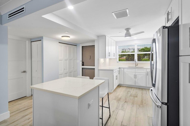 kitchen with stainless steel refrigerator, white cabinetry, a center island, ceiling fan, and light stone countertops