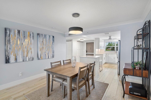 dining area featuring ornamental molding, a textured ceiling, and light wood-type flooring