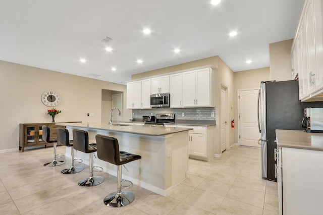 kitchen with a kitchen island with sink, sink, a breakfast bar area, white cabinetry, and stainless steel appliances