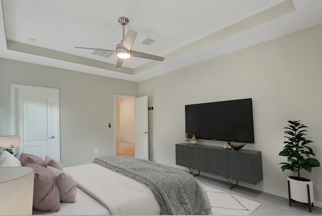 bedroom with ceiling fan, light colored carpet, and a tray ceiling