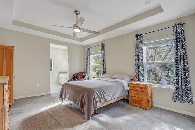 bedroom featuring ceiling fan, ensuite bath, and a tray ceiling