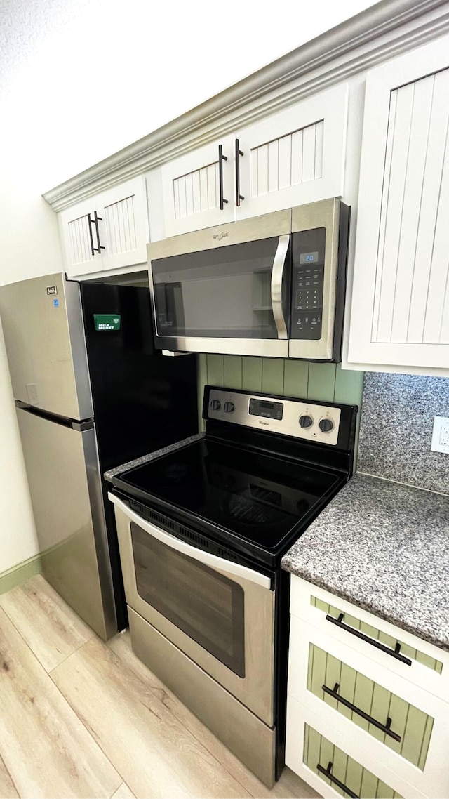 kitchen featuring appliances with stainless steel finishes, white cabinetry, tasteful backsplash, light hardwood / wood-style floors, and dark stone counters