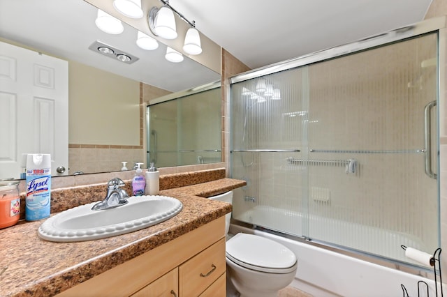 bathroom featuring toilet, bath / shower combo with glass door, and vanity