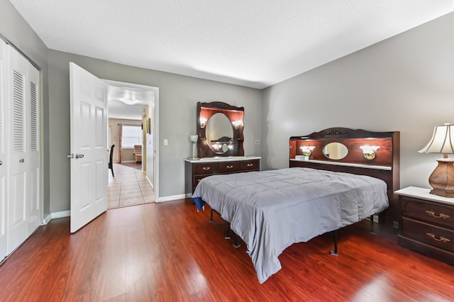 bedroom with a textured ceiling, a closet, wood finished floors, and baseboards