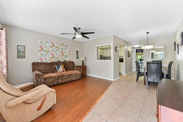 living room with ceiling fan, a textured ceiling, baseboards, and light tile patterned floors