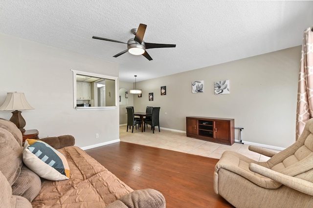 living room with ceiling fan, baseboards, a textured ceiling, and wood finished floors