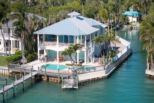 rear view of property with a swimming pool with hot tub, a water view, and a patio area