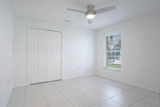 unfurnished bedroom with ceiling fan, light tile patterned flooring, a textured ceiling, and a closet