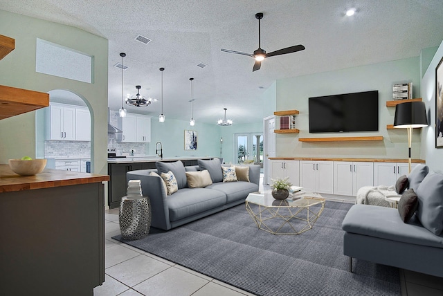 tiled living room with a textured ceiling, sink, high vaulted ceiling, and ceiling fan with notable chandelier