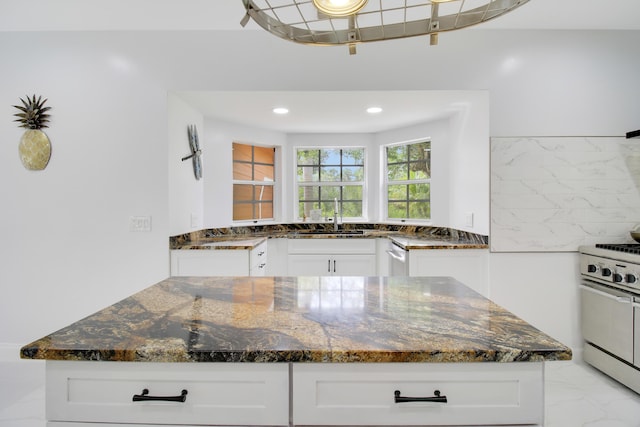 kitchen featuring stainless steel range, white cabinets, dark stone counters, and sink