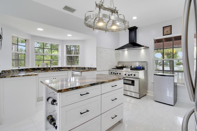 kitchen featuring wall chimney exhaust hood, dark stone countertops, decorative backsplash, white cabinets, and appliances with stainless steel finishes