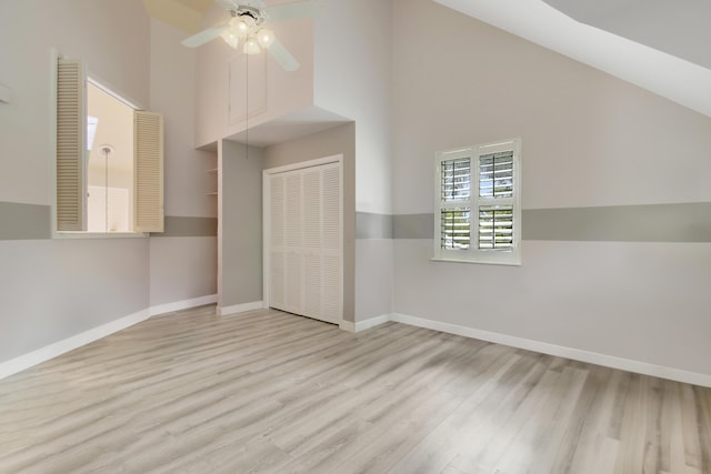 unfurnished bedroom with high vaulted ceiling, wood finished floors, a closet, baseboards, and ceiling fan