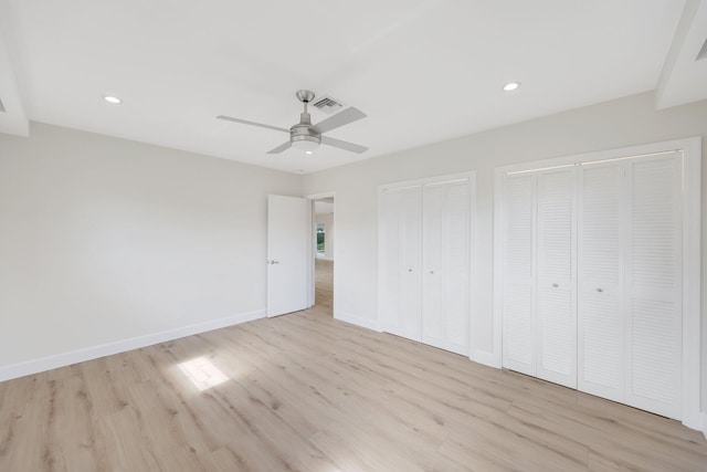 unfurnished bedroom featuring ceiling fan, light wood-type flooring, and two closets