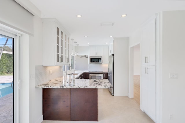 kitchen featuring white cabinetry, tasteful backsplash, light stone counters, kitchen peninsula, and appliances with stainless steel finishes