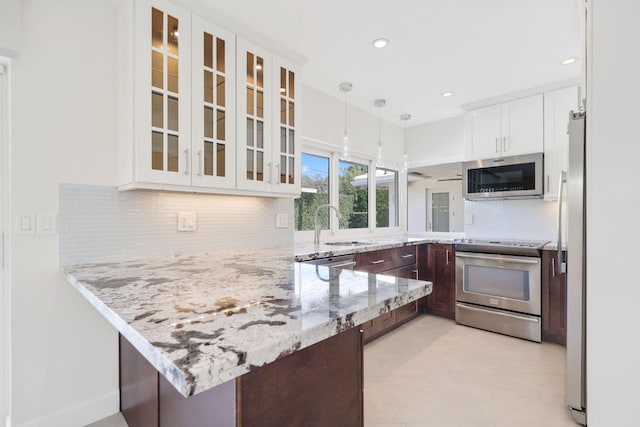 kitchen featuring pendant lighting, kitchen peninsula, appliances with stainless steel finishes, light stone counters, and white cabinetry