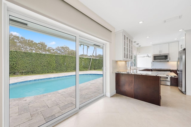 kitchen with white cabinets, light stone counters, kitchen peninsula, and stainless steel appliances