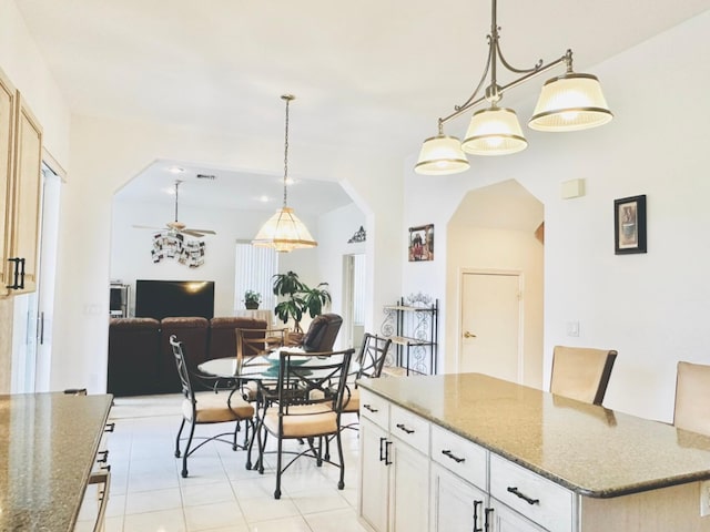 kitchen with ceiling fan, stone countertops, white cabinetry, a kitchen island, and hanging light fixtures