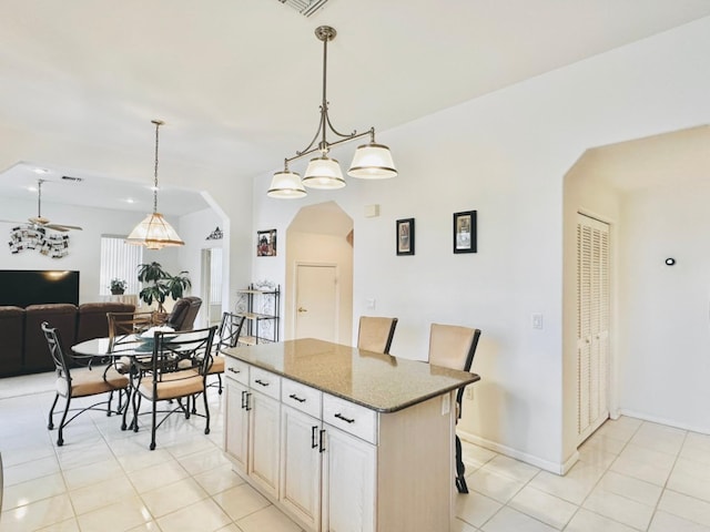 kitchen featuring ceiling fan, a center island, hanging light fixtures, a breakfast bar, and light tile patterned floors