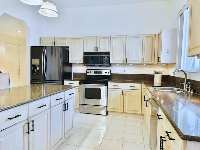 kitchen featuring appliances with stainless steel finishes, light tile patterned floors, dark stone countertops, and sink