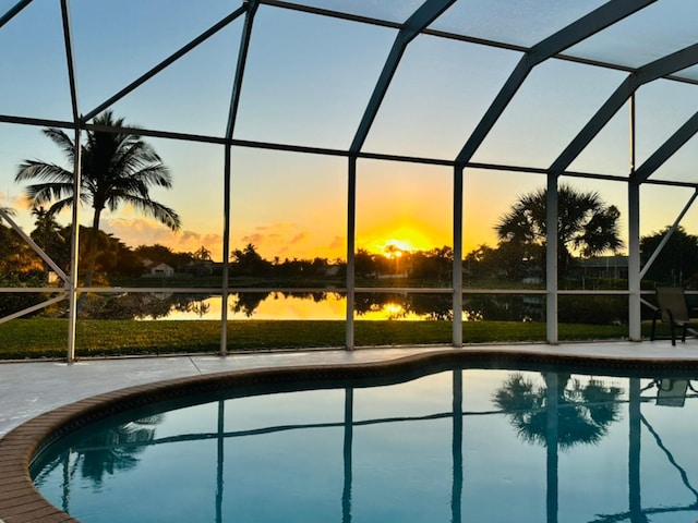 pool at dusk with a patio, a water view, and glass enclosure