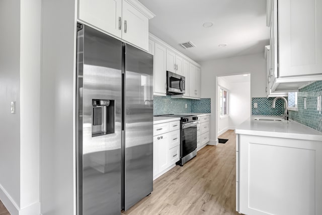 kitchen with white cabinets, sink, light wood-type flooring, tasteful backsplash, and stainless steel appliances