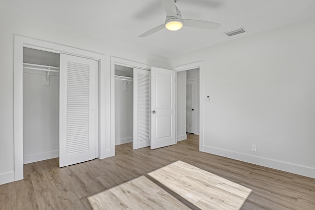 unfurnished bedroom with ceiling fan, light hardwood / wood-style floors, and two closets