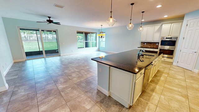 kitchen featuring tasteful backsplash, ceiling fan, sink, a center island with sink, and hanging light fixtures