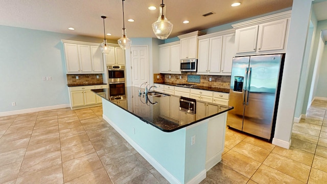 kitchen with appliances with stainless steel finishes, tasteful backsplash, sink, pendant lighting, and a center island with sink