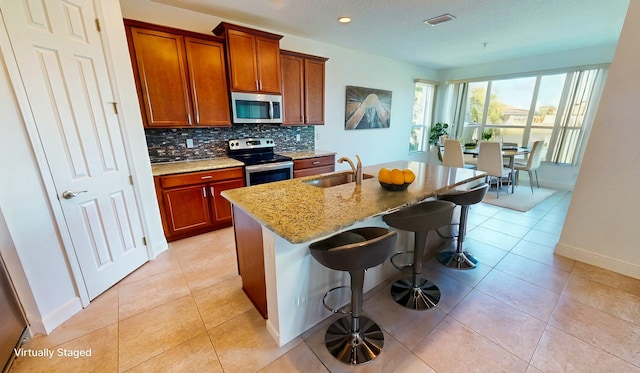 kitchen featuring light stone countertops, appliances with stainless steel finishes, a kitchen breakfast bar, sink, and a center island with sink