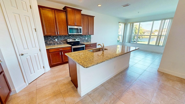 kitchen with light stone countertops, sink, stainless steel appliances, decorative backsplash, and a kitchen island with sink