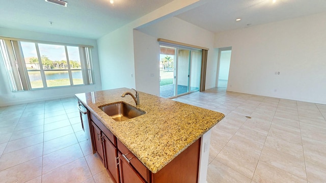 kitchen with sink, light stone countertops, an island with sink, and light tile patterned floors