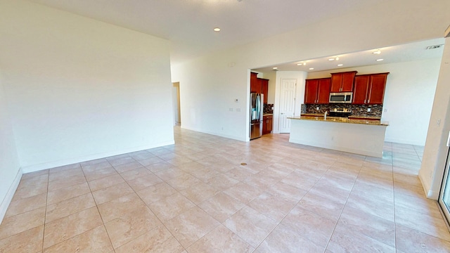 kitchen featuring backsplash, light tile patterned floors, stainless steel appliances, and a kitchen island with sink