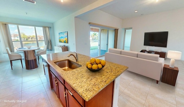 kitchen featuring light stone counters, sink, plenty of natural light, and an island with sink