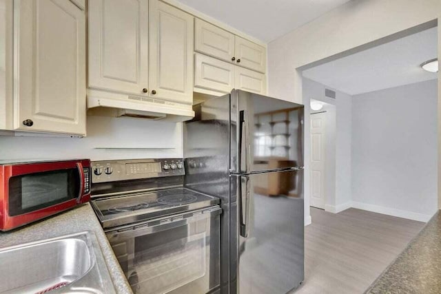 kitchen with sink, black range with electric cooktop, light hardwood / wood-style flooring, cream cabinets, and fridge