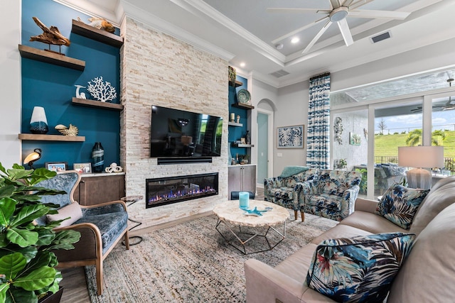 living room featuring built in shelves, ceiling fan, crown molding, hardwood / wood-style flooring, and a stone fireplace