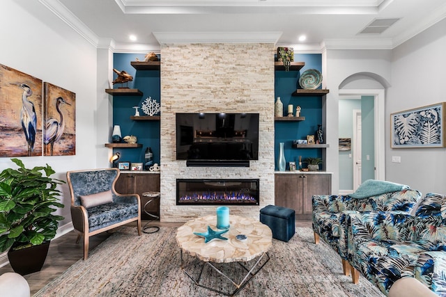 living room featuring hardwood / wood-style flooring, built in shelves, a stone fireplace, and crown molding