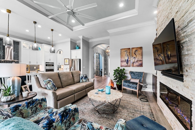 living room with hardwood / wood-style floors, a raised ceiling, a stone fireplace, crown molding, and ceiling fan