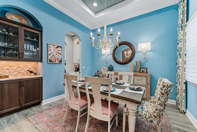 dining space featuring a chandelier, light wood-type flooring, a raised ceiling, and ornamental molding