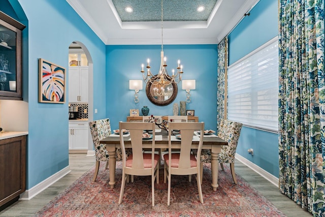 dining room with a raised ceiling, crown molding, a notable chandelier, and light wood-type flooring