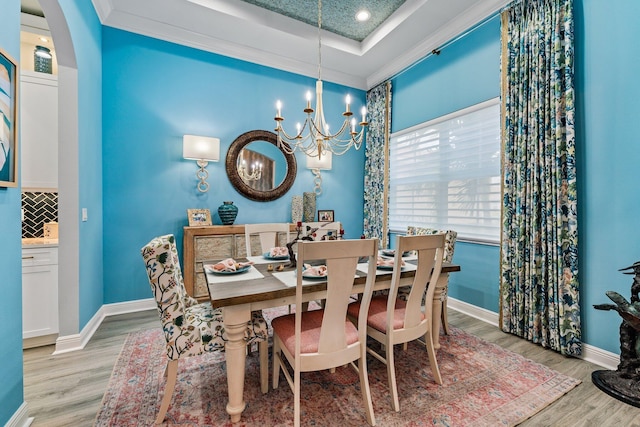 dining space featuring a tray ceiling, a chandelier, crown molding, and light hardwood / wood-style floors