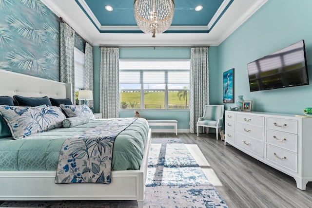 bedroom with light hardwood / wood-style floors, a raised ceiling, ornamental molding, and a chandelier