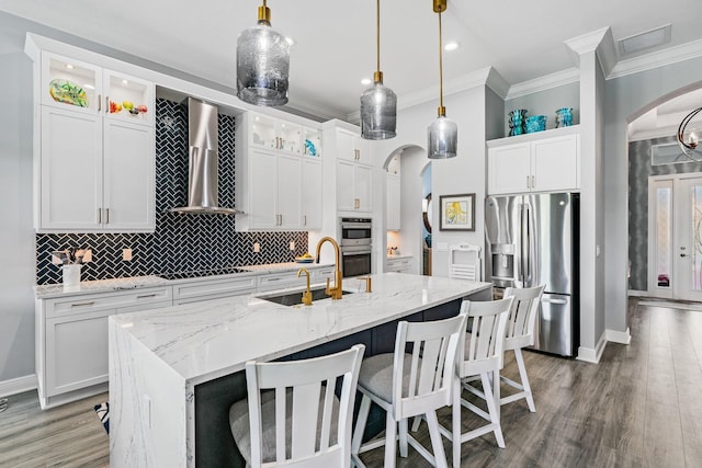 kitchen featuring a center island with sink, sink, hanging light fixtures, wall chimney exhaust hood, and stainless steel appliances