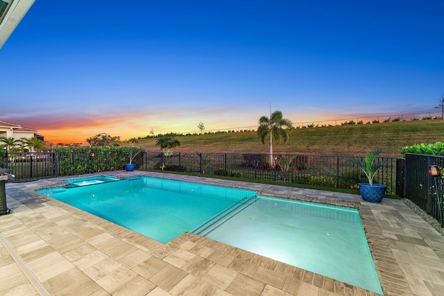 pool at dusk with a patio area, an in ground hot tub, and a rural view