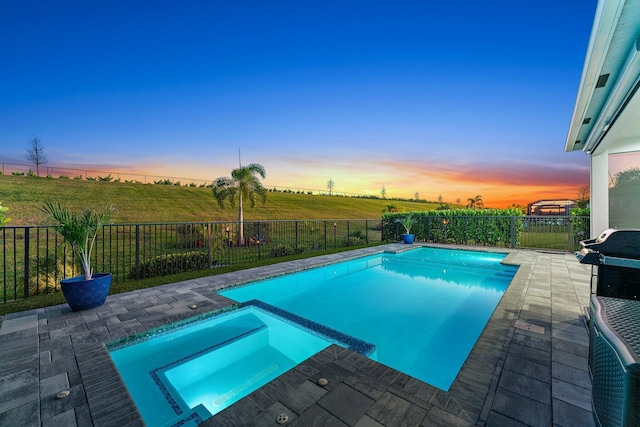 pool at dusk with a patio area and an in ground hot tub