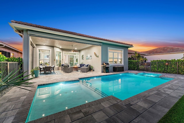 pool at dusk with an in ground hot tub, an outdoor hangout area, area for grilling, ceiling fan, and a patio area