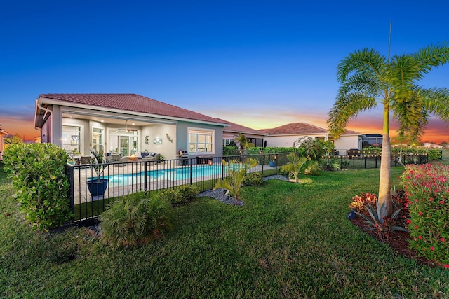 pool at dusk featuring a patio, ceiling fan, and a lawn